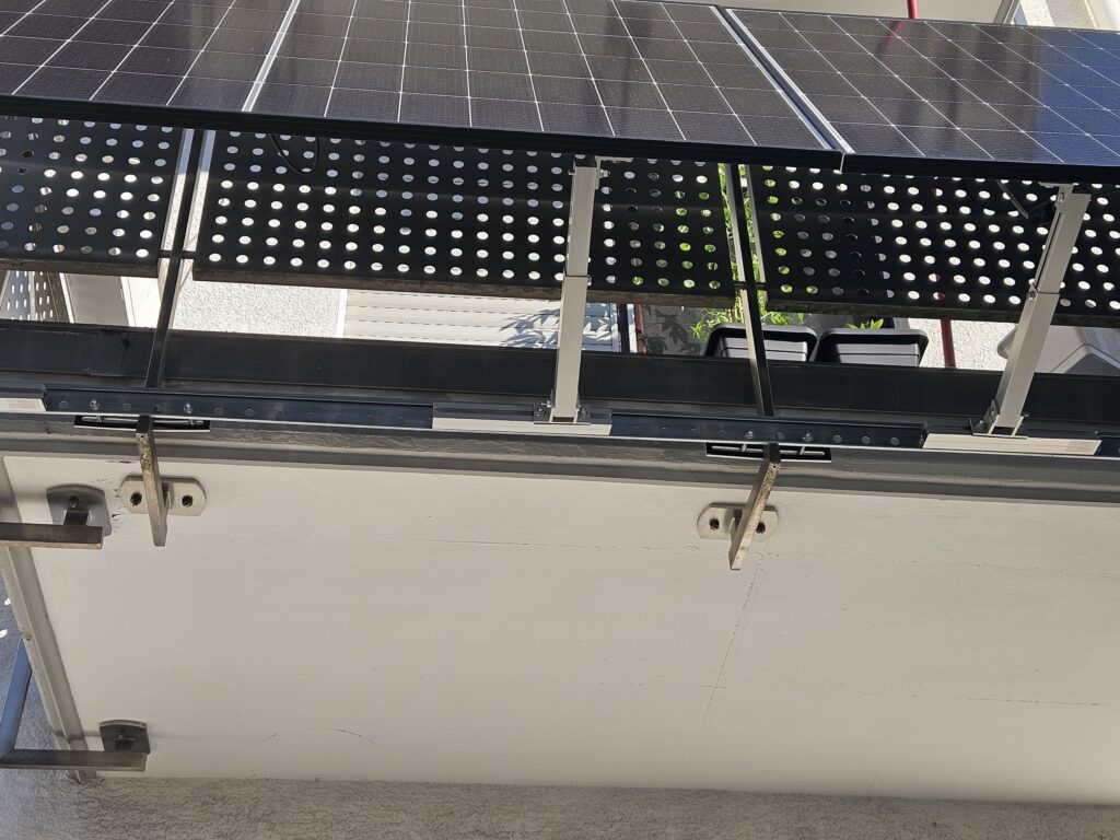 Untersicht eines Balkongeländers mit zwei montierten Solarmodulen. Sichtbar sind die Halterungen, die verlängerte Montageschiene sowie die Befestigungspunkte am Geländer.